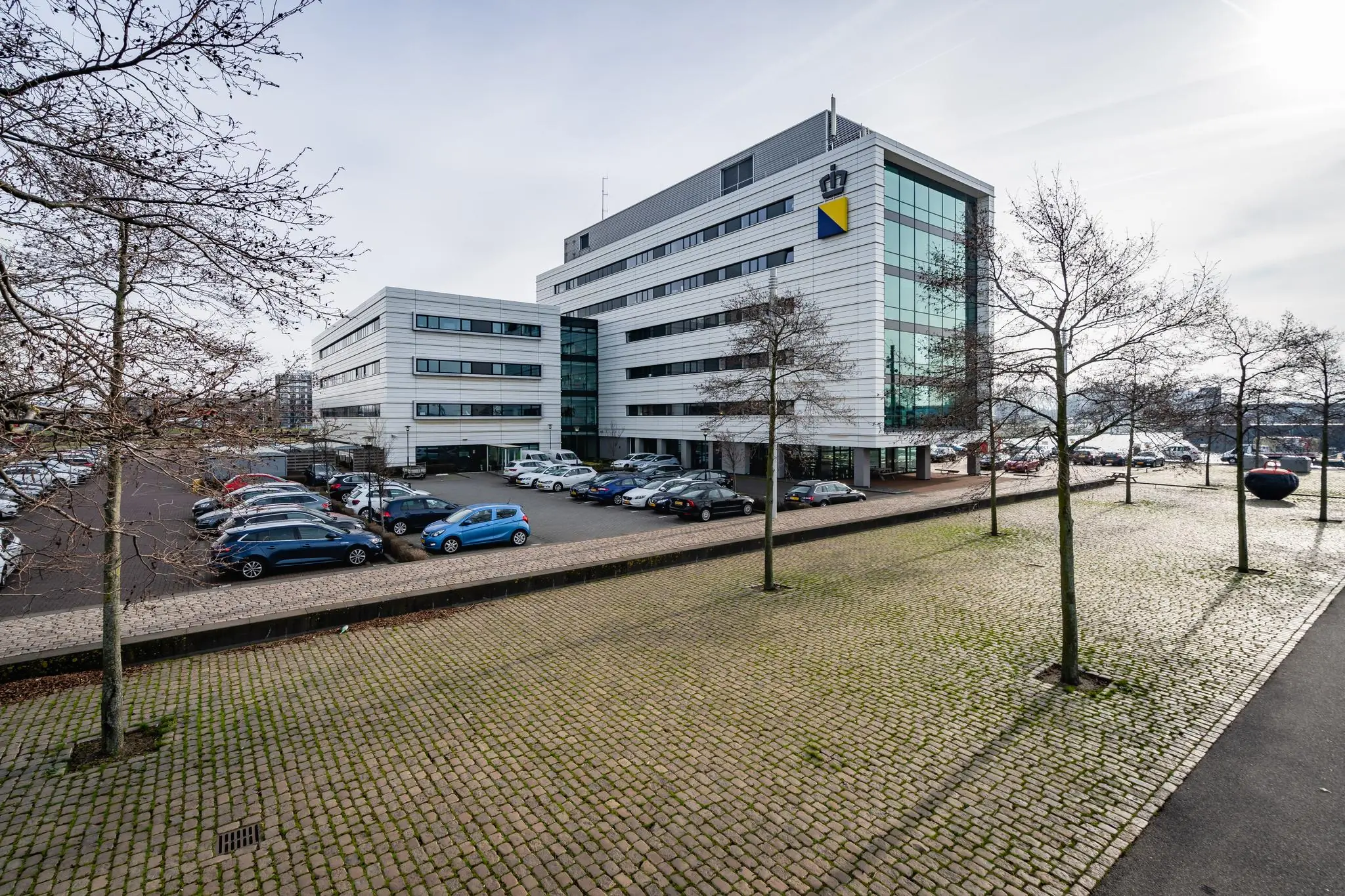 Modern kantoorgebouw aan de Waalhaven O.Z. in Rotterdam met parkeerplaats en omliggende bomen.